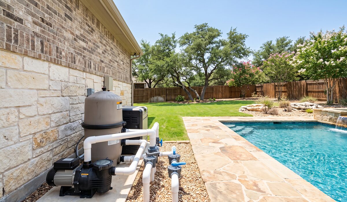 Pool equipment pad with pump, filter, and plumbing beside a Texas home