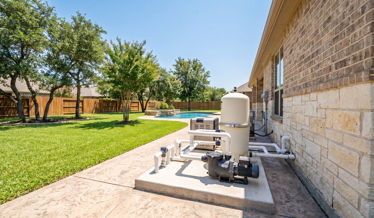 Pool equipment pad with pump, filter, and plumbing beside a Texas home